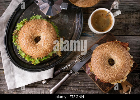 Zwei Bagels mit Eintopf Rindfleisch, frischem Salat, Speck, Rührei und gebratenen Zwiebeln serviert auf Vintage Metall Tablett mit Kaffee ein Stockfoto