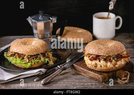 Zwei Bagels mit Eintopf Rindfleisch, frischem Salat, Speck, Rührei und gebratenen Zwiebeln serviert auf Vintage Metalltablett und Holz hacken b Stockfoto