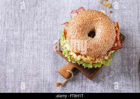 Bagel mit Eintopf Rindfleisch, frischem Salat und gebratenen Zwiebeln auf kleine hölzerne hacken an Bord über hölzerne Hintergrund. Ansicht von oben Stockfoto