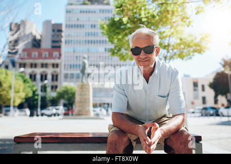 Porträt von schöner senior Mann sitzen im Freien. Ältere männliche Touristen mit Sonnenbrille draußen sitzen in der Stadt auf einem Sommer-da Stockfoto