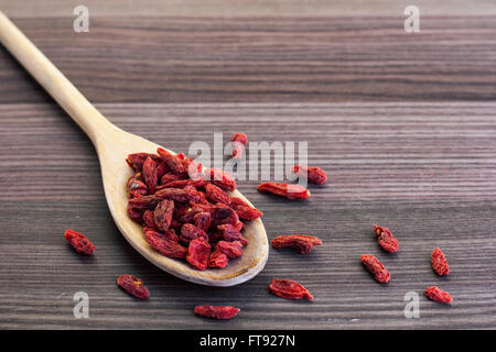 Getrocknete Goji-Beeren in einem Holzlöffel mit einer kleinen Tasse Tee auf der Seite Stockfoto