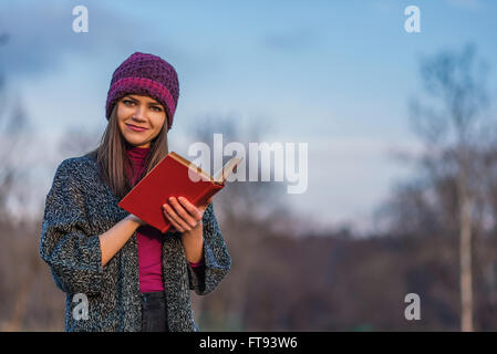 Ein Teenager-Mädchen in lila Hut Holding eröffnet Buch mit rotem Einband in einem Park aufhalten. Stockfoto