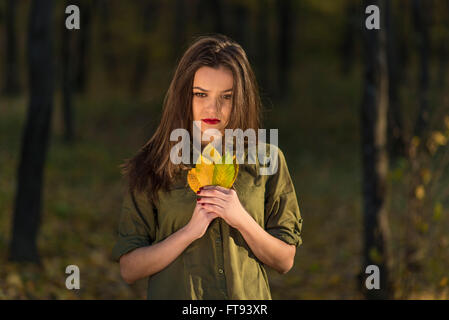 Nachdenklich Herbstlook. Ein meditativer Teenager-Mädchen ist in einem herbstlichen Wald nach unten während gelbe Blätter in ihren Händen hält. Stockfoto