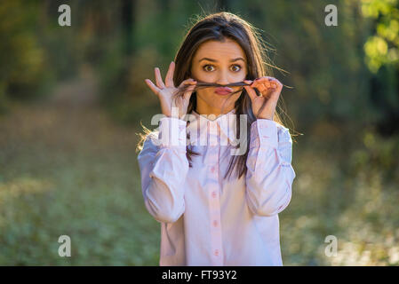 Ein junges Mädchen macht Schnurrbart aus ihrem Haar mit weit aufgerissenen Augen und einen skurrilen Ausdruck auf ihrem Gesicht. Stockfoto