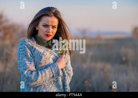 Kalt in einem Feld. Ein Teenager-Mädchen, eingehüllt in eine warme Jacke in einem Feld während des Sonnenuntergangs. Stockfoto