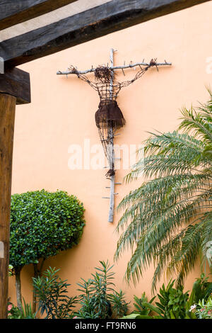 Skulptur von einer Kreuzigung. Eine Christusfigur altmodisch aus rostigen Stacheldraht wird auf einem rustikalen hölzernen Kreuz gehängt. Stockfoto