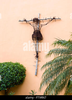 Skulptur von einer Kreuzigung. Eine Christusfigur altmodisch aus rostigen Stacheldraht wird auf einem rustikalen hölzernen Kreuz gehängt. Stockfoto