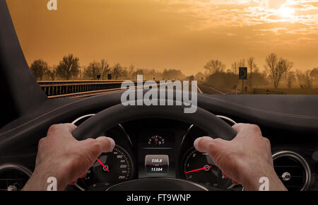 Das fahren bei Sonnenuntergang. Blick von der Fahrer-Winkel während Hände am Lenkrad. Stockfoto