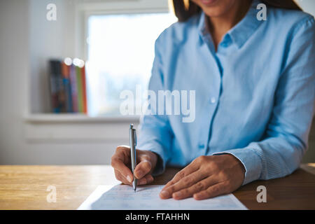 Geschäftsfrau, die auf ein Dokument zu schreiben, als sie an ihrem Schreibtisch im Büro sitzt Nahaufnahme von ihren Händen und den Stift Stockfoto