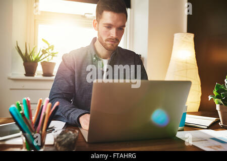 Besorgt Geschäftsmann Lesen von Daten auf seinem Laptop mit einem feierlichen Ausdruck, als er in seinem Home Office arbeitet, bunte lens flare Stockfoto