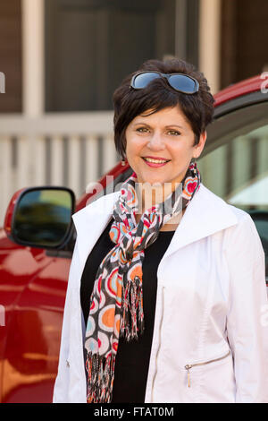 Porträt einer glücklich, selbstbewusst, Reife, mittleren Alters professionelle Frau stehend neben Auto in der Nähe ein Haus oder zu Hause Stockfoto