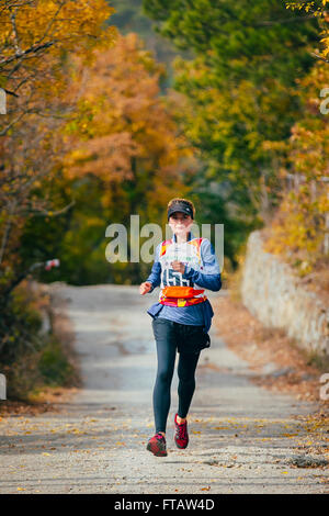 junge Frau läuft auf Straßenseite im herbstlichen Wald während Bergmarathon Stockfoto