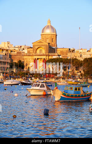 Die Ansicht der Kirche St. Joseph am Ufer und einer traditionellen maltesischen Boote (Luzzu) in der Bucht von Kalkara zwischen Birgu und Kalkara Stockfoto