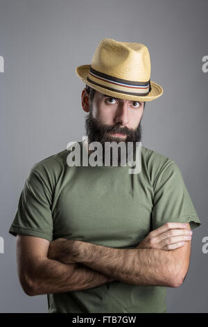 Ernsthafter unglücklicher bärtiger Mann mit Strohhut intensive finsteren Blick in die Kamera. Kopfschuss-Porträt über graue Studio-Hintergrund mit Vignette. Stockfoto