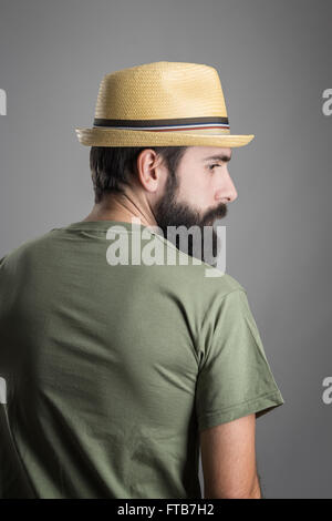 Rückansicht des jungen ernst bärtiger Mann mit Strohhut wegsehen. Kopfschuss-Porträt über graue Studio-Hintergrund mit Vignette. Stockfoto