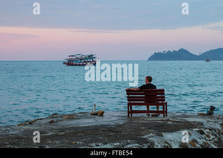 Einsamer Mann sitzt auf einer Bank an der Küste mit Blick auf das Meer. Stockfoto