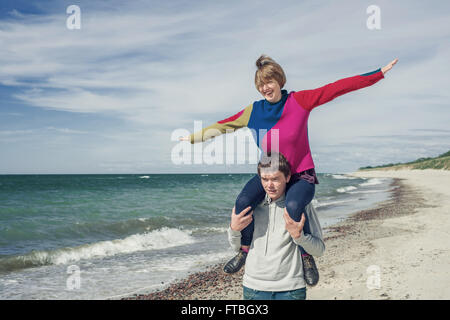 Mann trägt Frau auf seinen Schultern am Strand Stockfoto