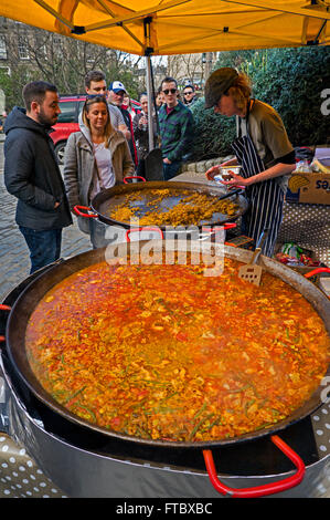 Ein junger Mann mit Paella in einem Stall in Stockbridge Sonntagsmarkt in Edinburgh. Stockfoto