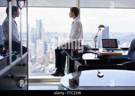 Erwachsenen Geschäftsmann am Schreibtisch im Büro sitzen und Blick aus dem Fenster, mit nachdenklichen Ausdruck. Der Mann betrachtet Stockfoto
