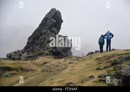 Zwei Fellwalkers durch die Haubitze oder Löwe und Lamm-Rock-Formation auf dem Gipfel Helm Felsen in der Nähe von Grasmere, Cumbria. UK Stockfoto