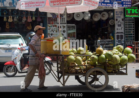 Ein Mann drängt eine Karre gewalkt mit Kokosnüssen, die er auf eine Stadt in Phnom Penh, Kambodscha Straße verkauft. Stockfoto