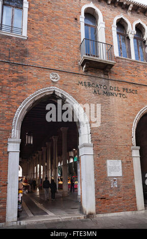 Kunstvoll verzierte neogotische Bogeneinfahrt zum gemauerten Fischmarkt, der das Säuleninnere und die Menschen im Mercato Rialto in Venedig, Italien, zeigt Stockfoto