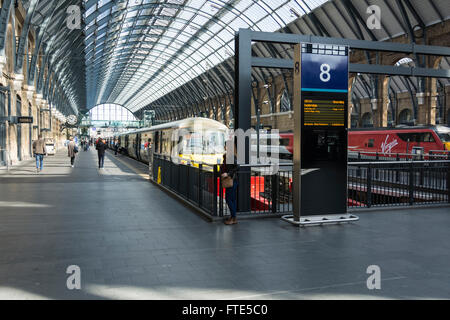 Eine Frau wartet, während Bahnreisenden am Kings Cross Bahnhof, London UK fahren Stockfoto