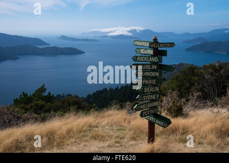 Ein Wegweiser zeigt Entfernungen an verschiedenen Orten mit der Marlborough Sounds im Hintergrund Stockfoto