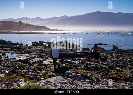 Menschen, die ihr Kanu über Felsen auf der Halbinsel in Kaikoura Stockfoto