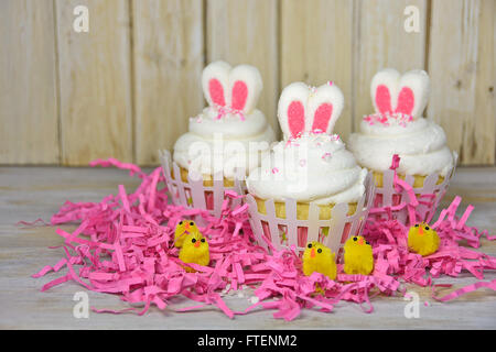 Marshmallow Hasenohren in Ostern Kuchen Glasur mit gelben Küken in rosa Papier Rasen. Stockfoto
