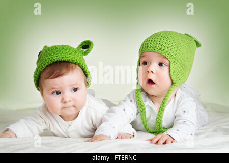 zwei niedliche Babys im Frosch Hüte auf Spft Decke liegend Stockfoto