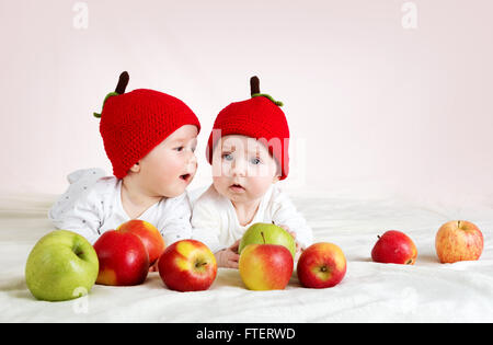 zwei niedliche Babys liegen in Hüte auf weichen Decke mit Äpfeln Stockfoto