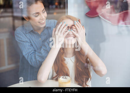 Attraktive junge Frau lächelnd bedeckte Augen durch Hände, fröhliche Rothaarige Mädchen sitzen im café Stockfoto