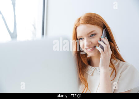 Glücklich nette junge Frau mit roten Haaren mit Laptop und Handy telefonieren im café Stockfoto