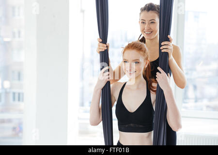 Lächelnde niedliche rothaarige junge Frau beim Antigravity Yoga im studio Stockfoto