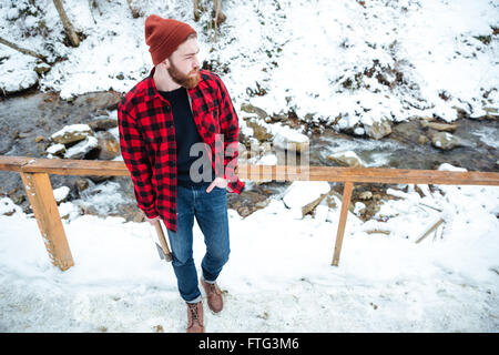 Draufsicht der hübschen nachdenklichen jungen Mann mit Axt stehen und blickte auf kleinen Bergfluss Stockfoto