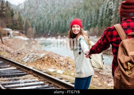 Glückliches junges Paar mit Rucksäcken, Hand in Hand und zu Fuß entlang der Bahn in Bergen Stockfoto