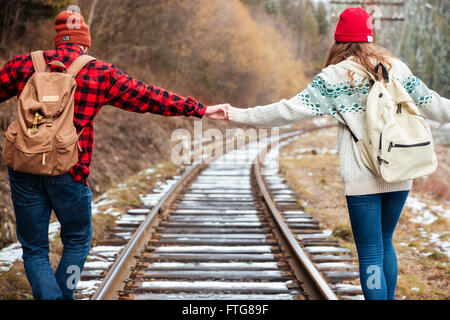 Schöne junge Paar mit Rucksäcke Hand in Hand und Wandern entlang der Eisenbahn zusammen Stockfoto