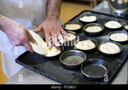 Bäcker Backwaren in einer Bäckerei Füllung Metall Ofen macht Dosen auf einem Tablett zum Backen mit rohen Teig, Nahaufnahme von seinen Händen Stockfoto