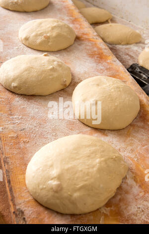 Hohen Winkel nahe Ansicht von einzelnen Brot Brötchen steigt auf rustikalen Holz Mehl gedeckten Tisch inmitten der Großbäckerei Stockfoto