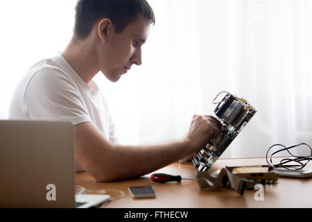 Porträt von hübschen jungen Computer Mechaniker mit defekten pc-Teile drinnen im home Office arbeiten Stockfoto