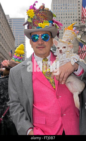 Ein Mann in einer seltsamen Hut & rosa Weste mit seinem weißen kleinen Hund auf der Fifth Avenue in Manhattan für die Osterparade. Stockfoto