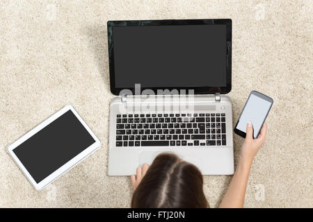 Frau mit Gerät-Bildschirmen, die auf dem Boden zu Hause arbeiten Stockfoto