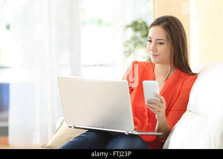 Unternehmer-Frau mit Laptop und Handy sitzen auf einer Couch zu Hause arbeiten Stockfoto