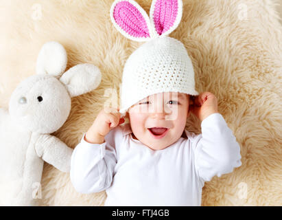 ein Jahr altes Baby liegend in Hase Hut auf Lamm Wolle Stockfoto