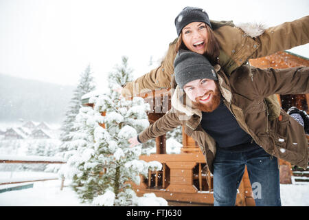 Happy gut aussehend bärtigen Mann Piggibacking, seine Freundin und Lachen im winter Stockfoto