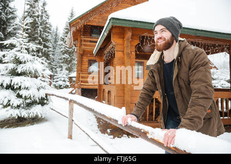 Porträt von fröhlich schön bärtigen Mann stand vor Holzhaus im Winterwald Stockfoto