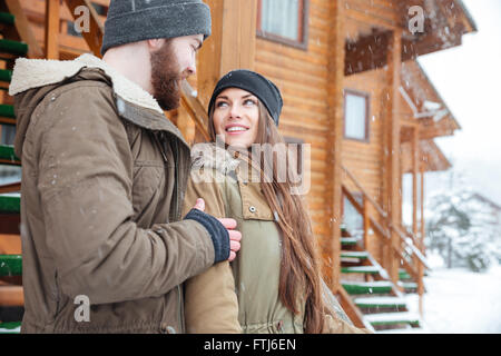 Schöne junge Paar stehen und sahen einander nahe Holzhütte im winter Stockfoto