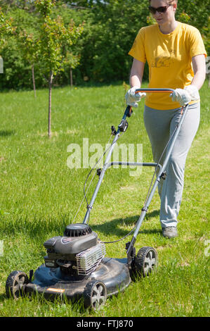 Junge Frau im Garten Rasen trimmen Rasenmäher schieben Stockfoto