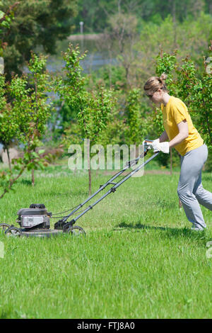 Junge Frau im Garten Rasen trimmen Rasenmäher schieben Stockfoto